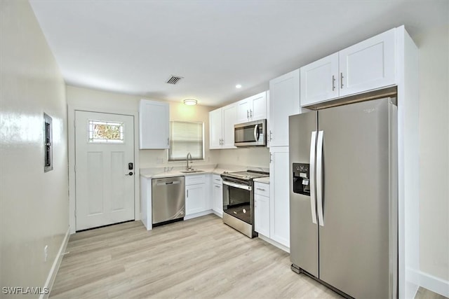 kitchen featuring light wood finished floors, visible vents, appliances with stainless steel finishes, white cabinetry, and a sink