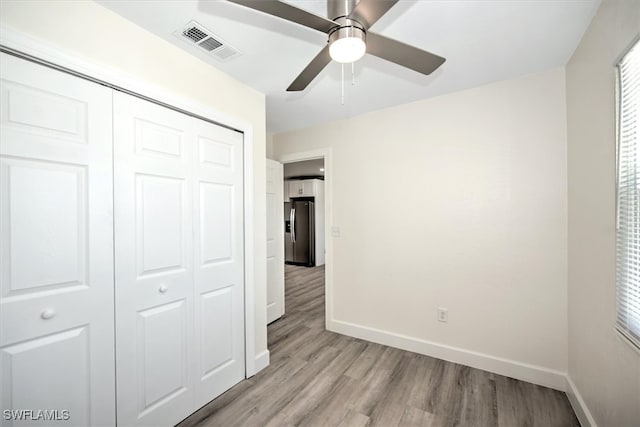 unfurnished bedroom with light hardwood / wood-style flooring, ceiling fan, a closet, and stainless steel refrigerator with ice dispenser