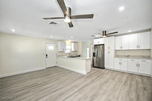 kitchen with visible vents, light wood-type flooring, light countertops, stainless steel fridge, and white cabinetry