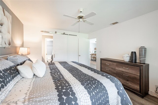 bedroom featuring visible vents, a barn door, wood finished floors, and ceiling fan