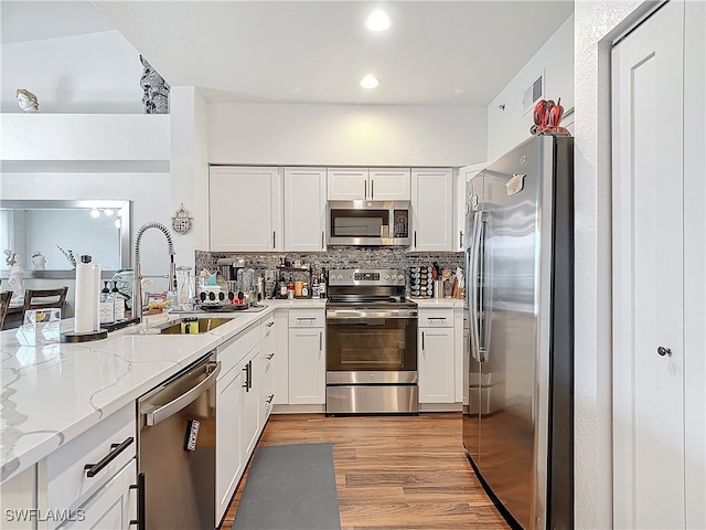 kitchen featuring light stone counters, stainless steel appliances, light hardwood / wood-style floors, white cabinetry, and decorative backsplash