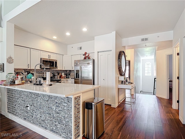 kitchen featuring dark hardwood / wood-style floors, backsplash, appliances with stainless steel finishes, kitchen peninsula, and white cabinets