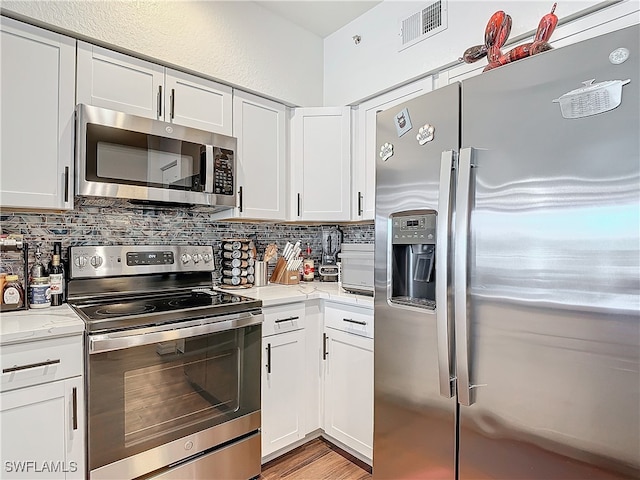 kitchen with backsplash, appliances with stainless steel finishes, light stone counters, light wood-type flooring, and white cabinets