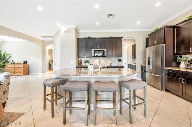 kitchen with crown molding, appliances with stainless steel finishes, light stone countertops, and an island with sink