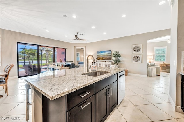 kitchen featuring sink, light tile patterned floors, dishwasher, light stone countertops, and an island with sink