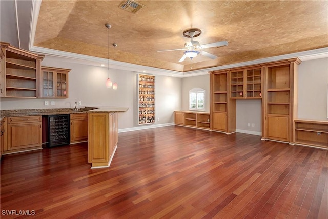 unfurnished living room featuring dark hardwood / wood-style flooring, a raised ceiling, beverage cooler, crown molding, and ceiling fan