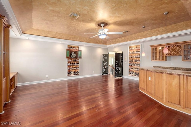 unfurnished living room featuring ceiling fan, dark hardwood / wood-style floors, crown molding, indoor bar, and a tray ceiling