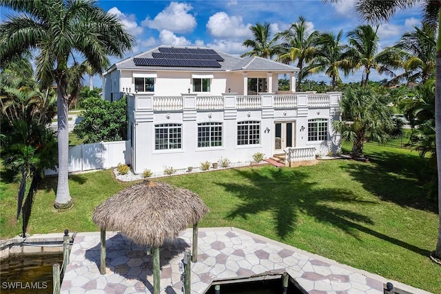 back of house with solar panels, a patio area, and a lawn