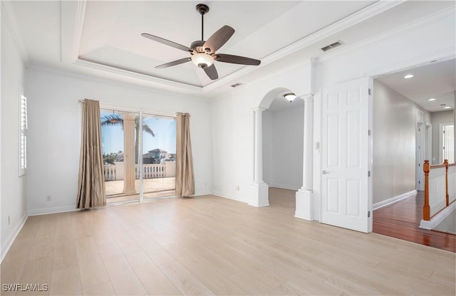 spare room with decorative columns, a tray ceiling, ceiling fan, crown molding, and light hardwood / wood-style flooring