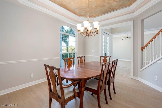 dining room with a tray ceiling, crown molding, light wood-style flooring, an inviting chandelier, and baseboards