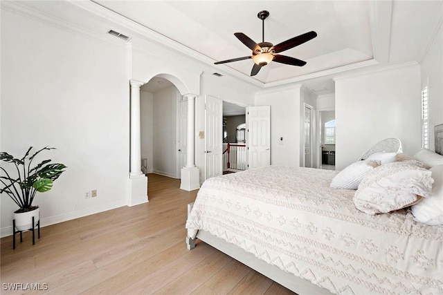 bedroom with light wood finished floors, decorative columns, visible vents, a raised ceiling, and ornamental molding