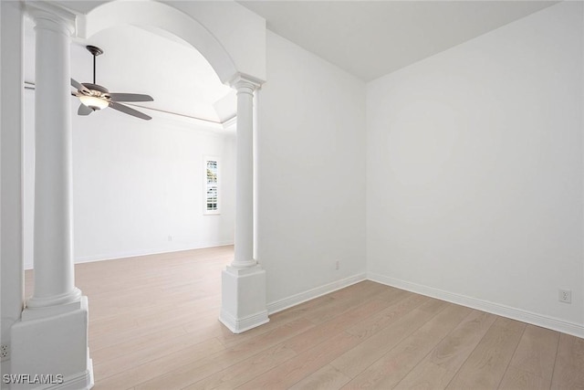 spare room with a ceiling fan, arched walkways, light wood-style flooring, and ornate columns