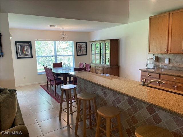 kitchen featuring light tile patterned floors, decorative light fixtures, sink, decorative backsplash, and a breakfast bar