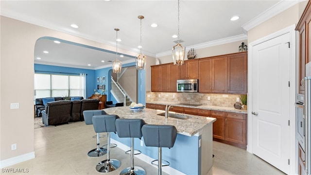 kitchen with a kitchen island with sink, ornamental molding, sink, and light stone countertops