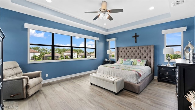 bedroom with multiple windows, ceiling fan, a raised ceiling, and wood-type flooring