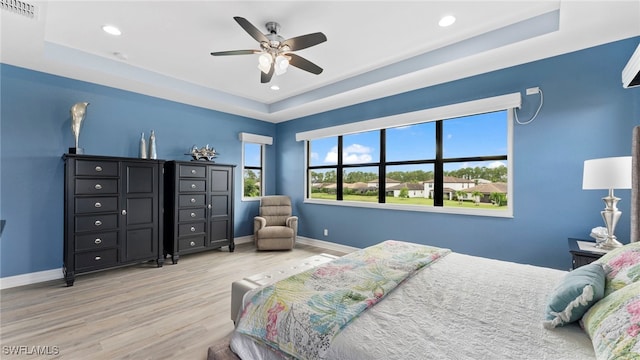 bedroom featuring a raised ceiling, ceiling fan, and light wood-type flooring