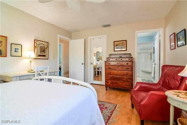 bedroom featuring a textured ceiling, light hardwood / wood-style flooring, ceiling fan, and connected bathroom