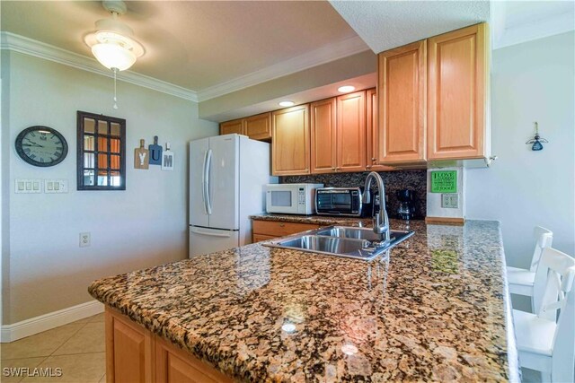 kitchen featuring dark stone counters, white appliances, light tile patterned floors, kitchen peninsula, and sink