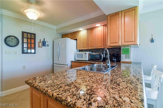 kitchen with white appliances, dark stone counters, a peninsula, ornamental molding, and decorative backsplash