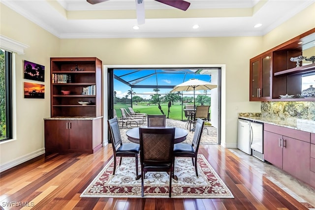 dining room featuring a tray ceiling, a healthy amount of sunlight, a ceiling fan, and a sunroom