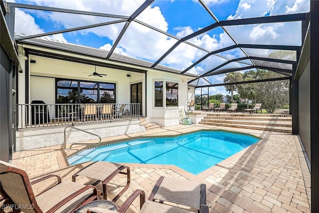 outdoor pool featuring glass enclosure, a ceiling fan, and a patio