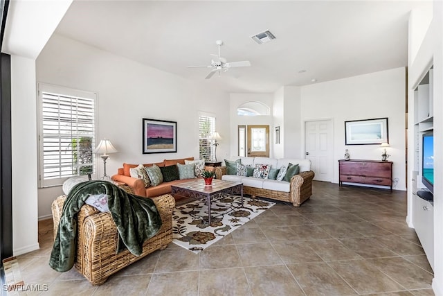 living area featuring tile patterned floors, visible vents, ceiling fan, and a towering ceiling