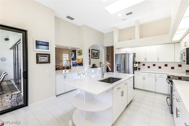 kitchen featuring open shelves, light countertops, appliances with stainless steel finishes, arched walkways, and a sink