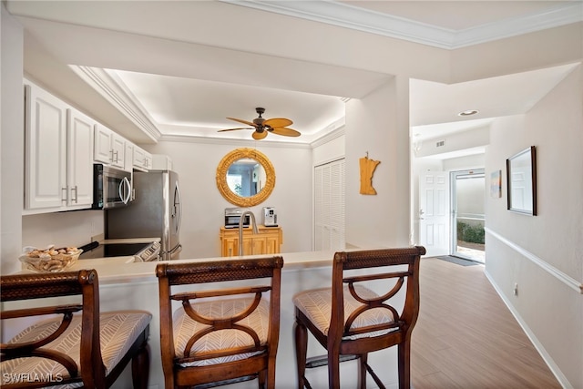 kitchen with appliances with stainless steel finishes, a kitchen bar, kitchen peninsula, ceiling fan, and light wood-type flooring