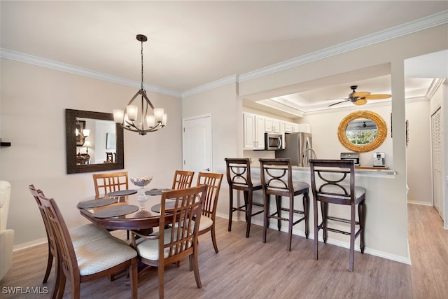 dining room featuring light wood-type flooring, a tray ceiling, ceiling fan with notable chandelier, and ornamental molding