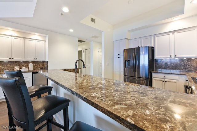 kitchen featuring dark stone countertops, kitchen peninsula, stainless steel fridge with ice dispenser, and tasteful backsplash