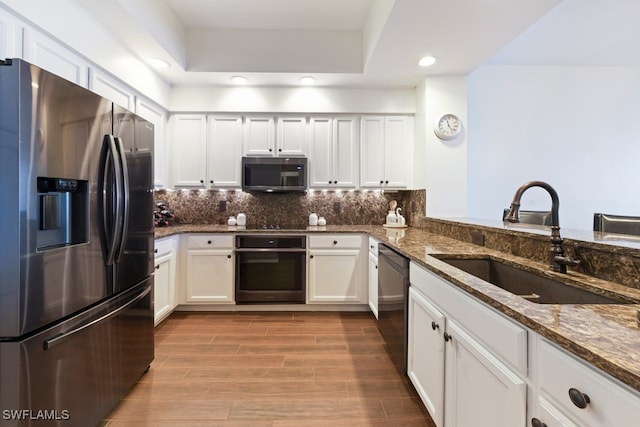 kitchen featuring light wood-type flooring, dark stone counters, black appliances, sink, and white cabinets