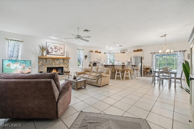 living room featuring a stone fireplace, light tile patterned floors, and ceiling fan with notable chandelier