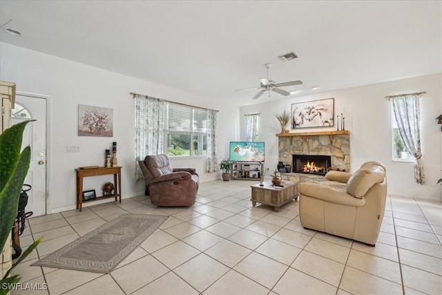 tiled living room with ceiling fan and a stone fireplace