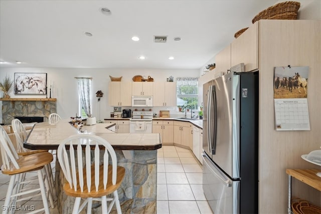 kitchen featuring white appliances, tile counters, a stone fireplace, a breakfast bar area, and light tile patterned flooring