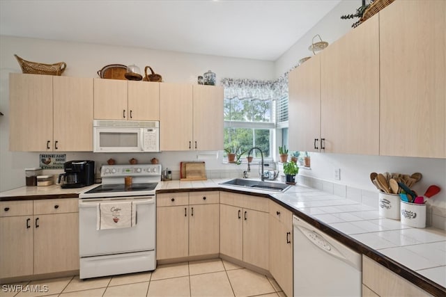 kitchen featuring light tile patterned floors, white appliances, sink, light brown cabinets, and tile counters