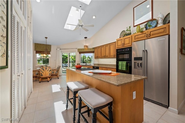 kitchen featuring a breakfast bar area, double oven, lofted ceiling with skylight, high end refrigerator, and light tile patterned flooring