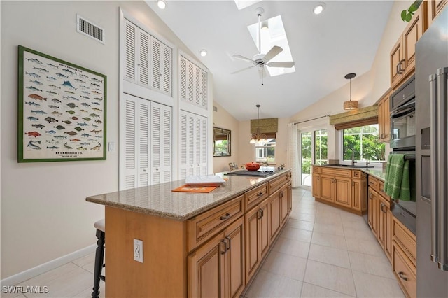 kitchen featuring a center island, a kitchen bar, light tile patterned floors, vaulted ceiling with skylight, and pendant lighting