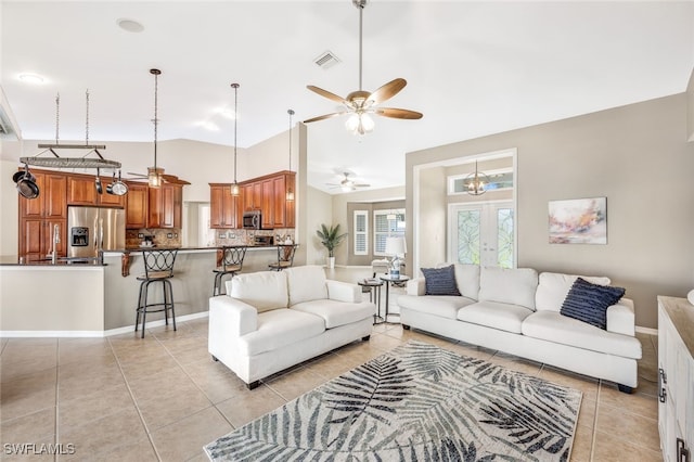 tiled living room featuring ceiling fan with notable chandelier, high vaulted ceiling, and french doors