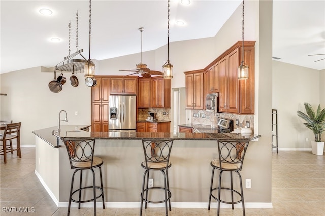 kitchen with dark stone counters, lofted ceiling, kitchen peninsula, appliances with stainless steel finishes, and ceiling fan