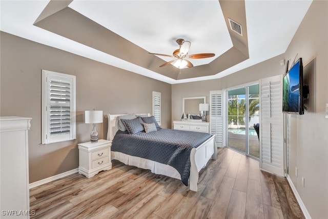 bedroom featuring access to outside, light wood-type flooring, a raised ceiling, and ceiling fan