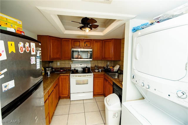 kitchen featuring a raised ceiling, stacked washer and dryer, ceiling fan, decorative backsplash, and appliances with stainless steel finishes