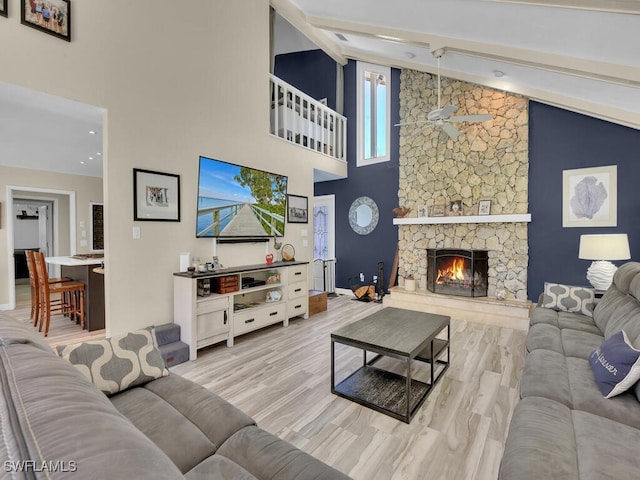 living room featuring light hardwood / wood-style flooring, high vaulted ceiling, and a stone fireplace