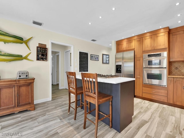 kitchen featuring a center island, a breakfast bar area, decorative backsplash, light hardwood / wood-style flooring, and appliances with stainless steel finishes