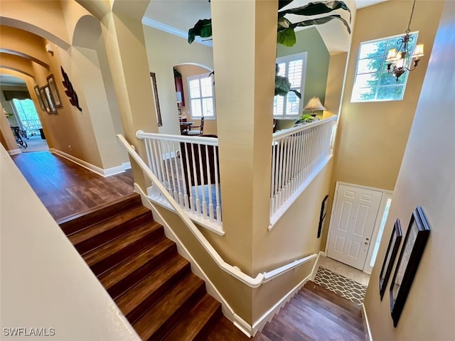 staircase with crown molding, a towering ceiling, hardwood / wood-style floors, and a notable chandelier