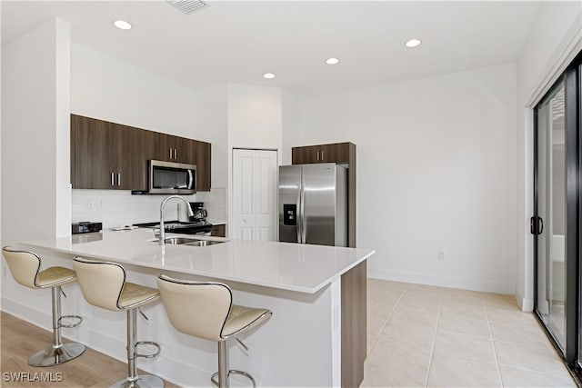 kitchen with light tile patterned floors, kitchen peninsula, stainless steel appliances, a breakfast bar area, and decorative backsplash