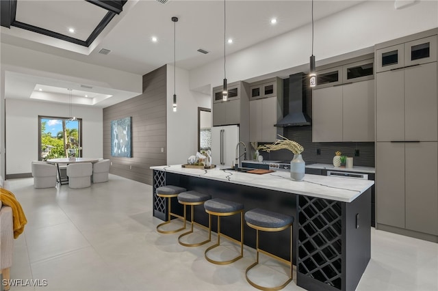 kitchen featuring a large island, light stone counters, hanging light fixtures, a tray ceiling, and wall chimney range hood