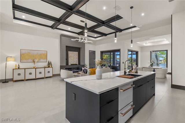 kitchen featuring decorative light fixtures, coffered ceiling, a kitchen island with sink, and sink