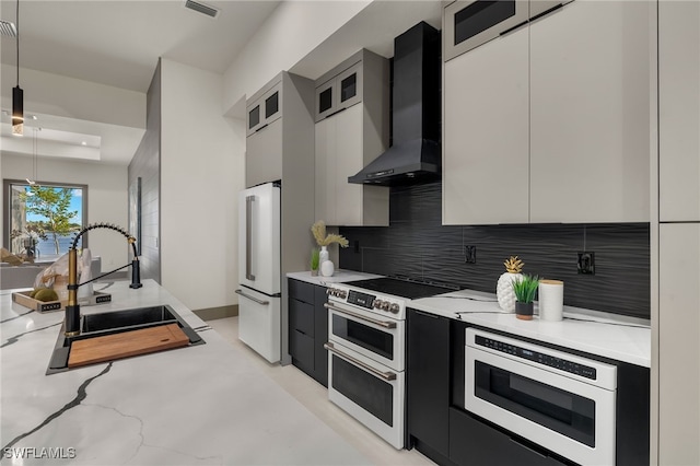 kitchen featuring white appliances, backsplash, hanging light fixtures, sink, and wall chimney range hood