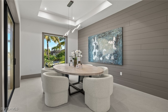 dining room with a raised ceiling and wood walls