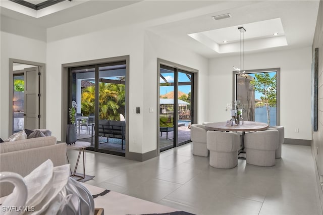 dining space featuring a water view, light tile patterned floors, and a raised ceiling